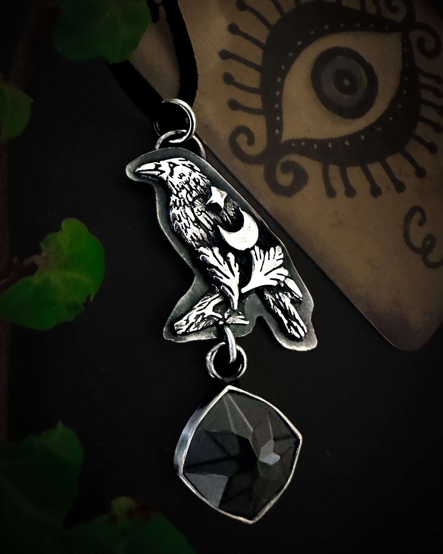 Handmade silver crow pendant featuring mystical designs and an engraved spinel gemstone.