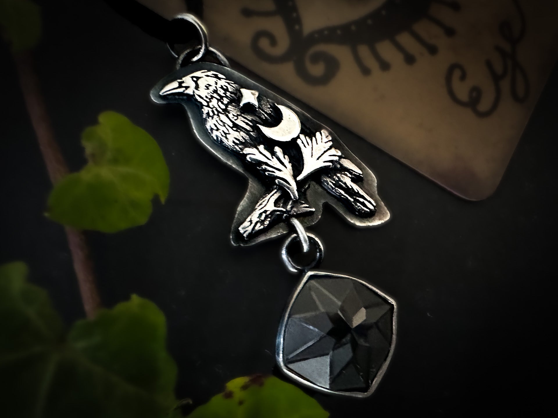 Sterling silver crow pendant with engraved spinel, crescent moon, star, and fern motifs. Handmade in sterling silver.