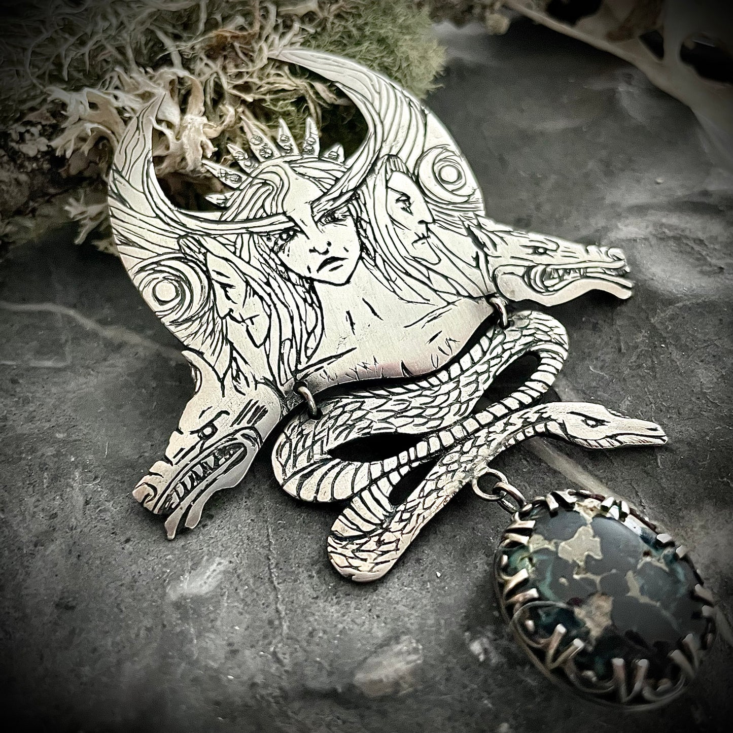 Hecate in triple goddess form, with her diadem and hounds either side. Serpent sits below and a Blue Boy variscite hangs from the piece. The shape in reminiscent of a crescent moon. Handmade by Silver Labyrinth Jewelry.