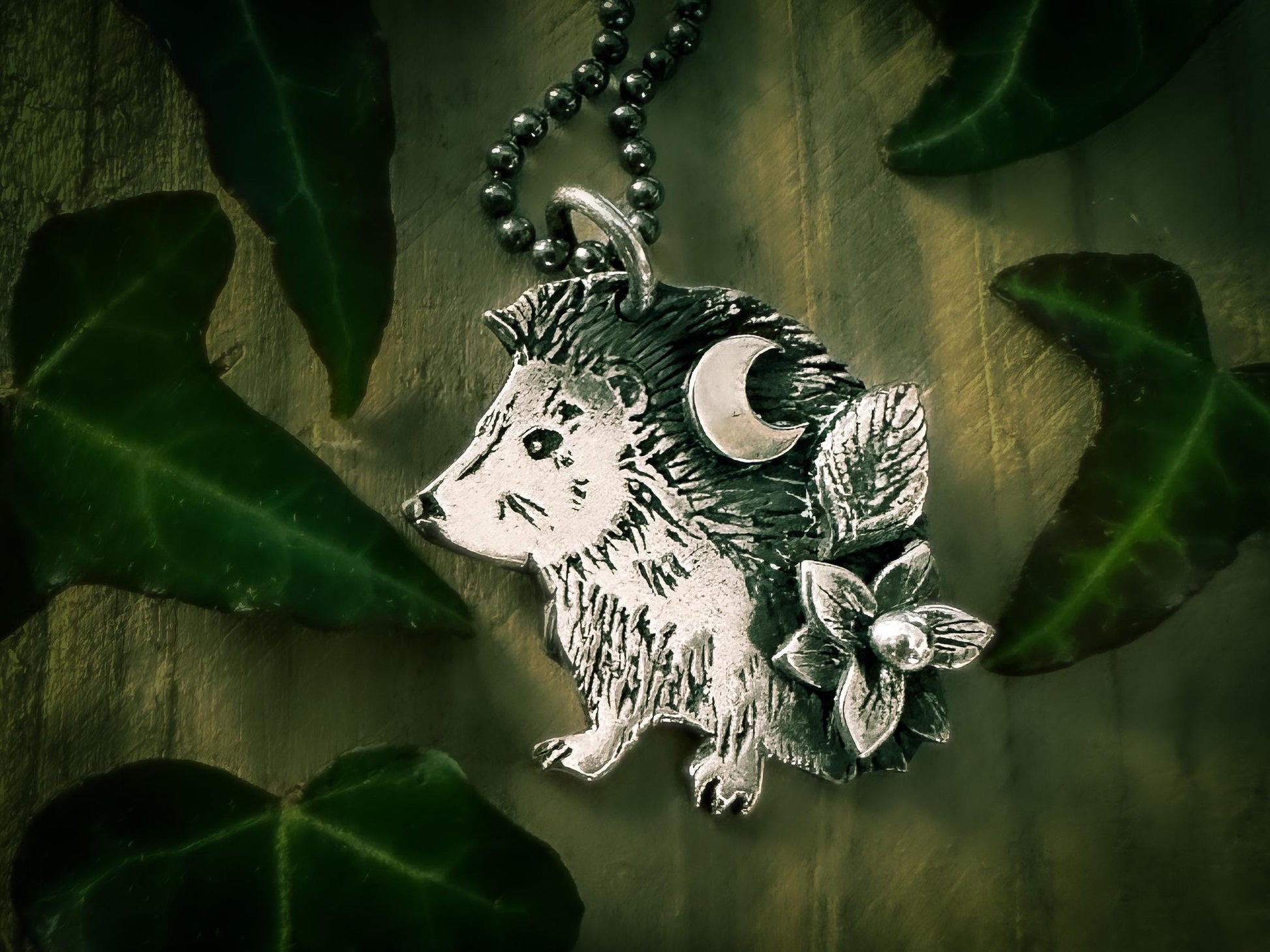 Detail of sterling silver little hedgehog pendant, shown with optional chain. Detailed with a flower, a leaf and a sickle moon. Handmade by Silver Labyrinth Jewelry