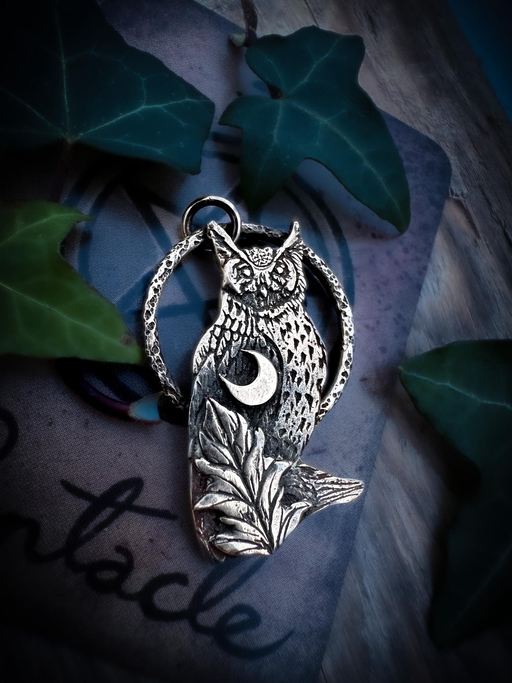 A detailed, handmade horned owl in sterling silver with a crescent moon and leaf