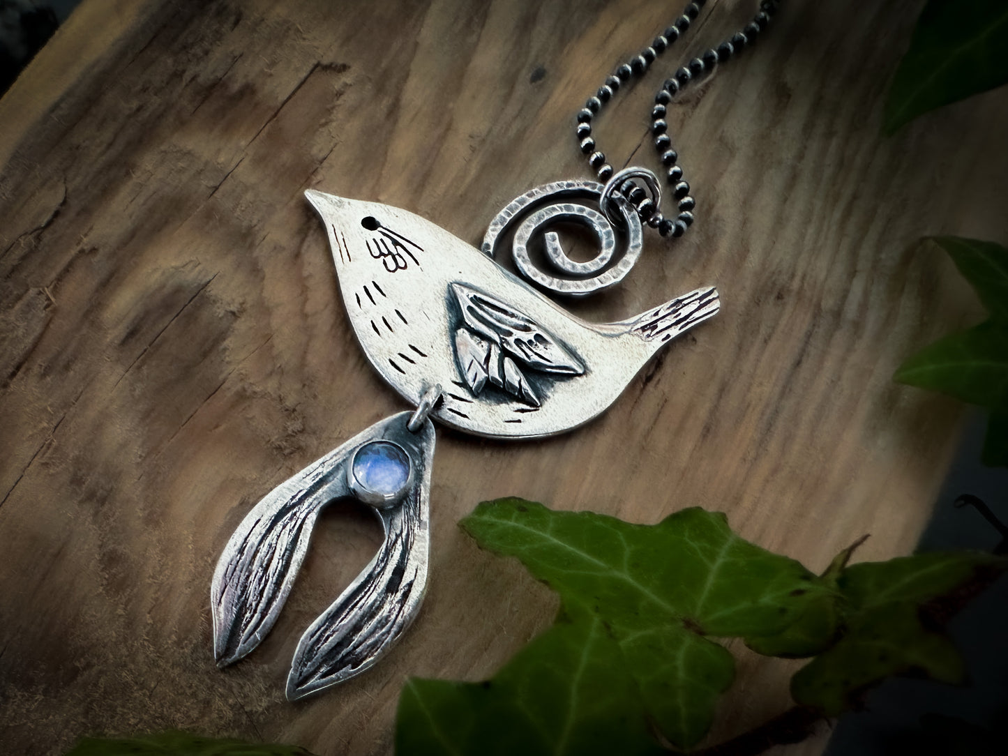 Side view of Wren and mistletoe necklace showing the beautiful details. A softly glowing moonstone sits on a mistletoe leaf. Inspired by Celtic folklore and the winter solstice, Yule. Handmade in sterling silver by Silver Labyrinth Jewelry