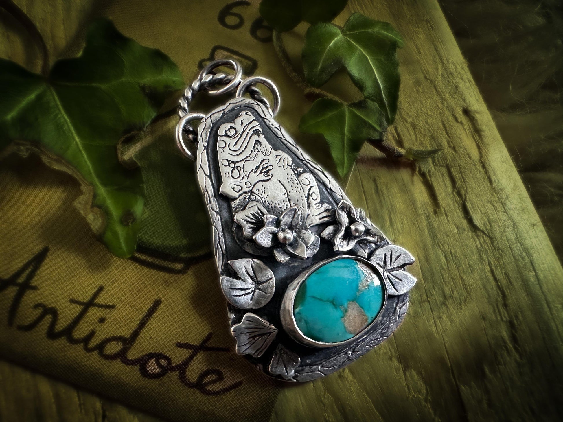 Finely detailed toad and natural Carico Lake turquoise pendant, with lily flowers and lily pads. On the back is a cauldron and a labyrinth. handmade in sterling silver. silverlabyrinthjewelry.com