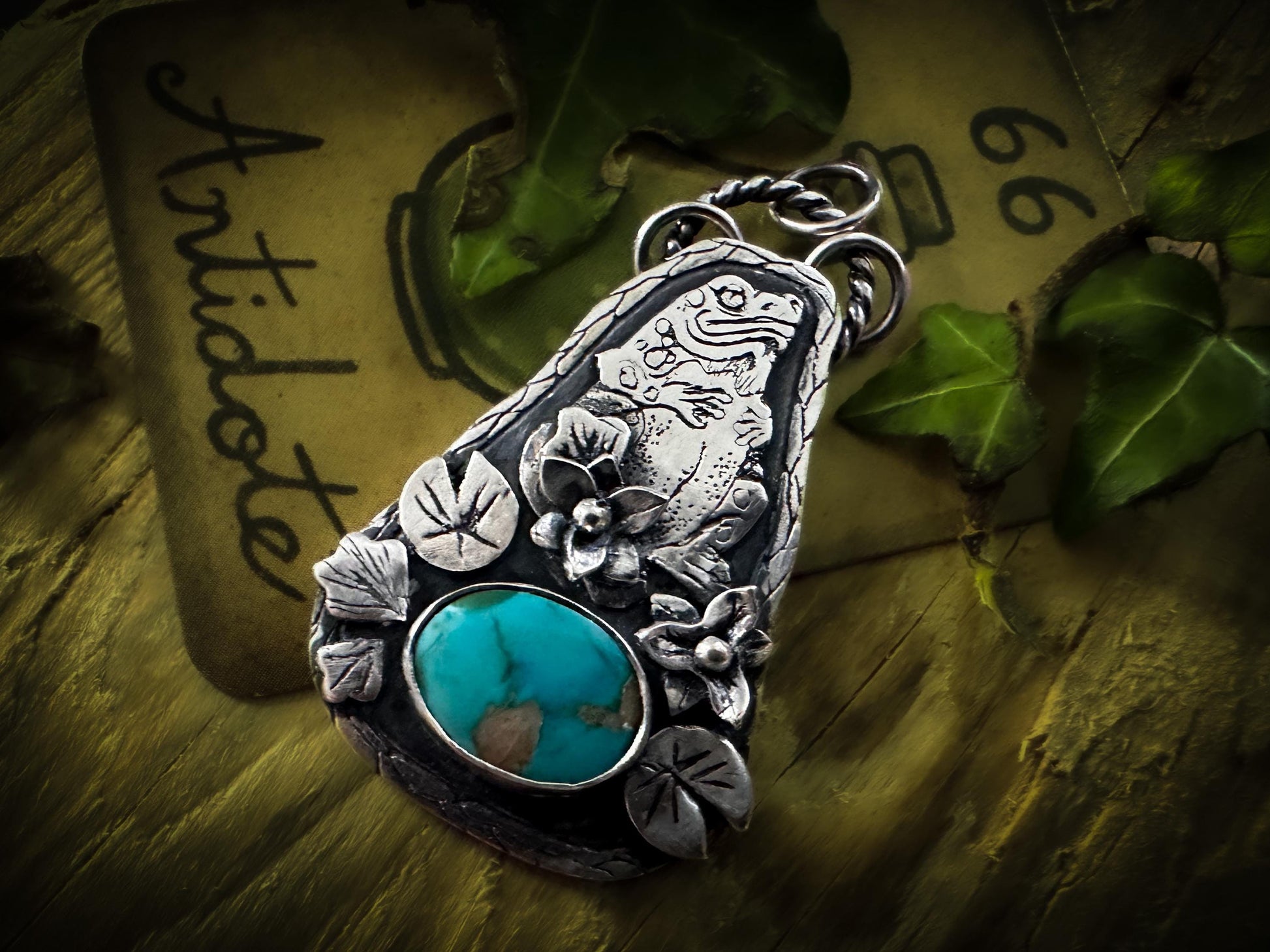 View from the right. A detailed Toad pendant with witchy detai silver piece, fine details, patina and polish. A vivid turquoise gemstone from the Carico Lake Mine in the US is set under the toad. By Silver Labyrinth Jewelry.