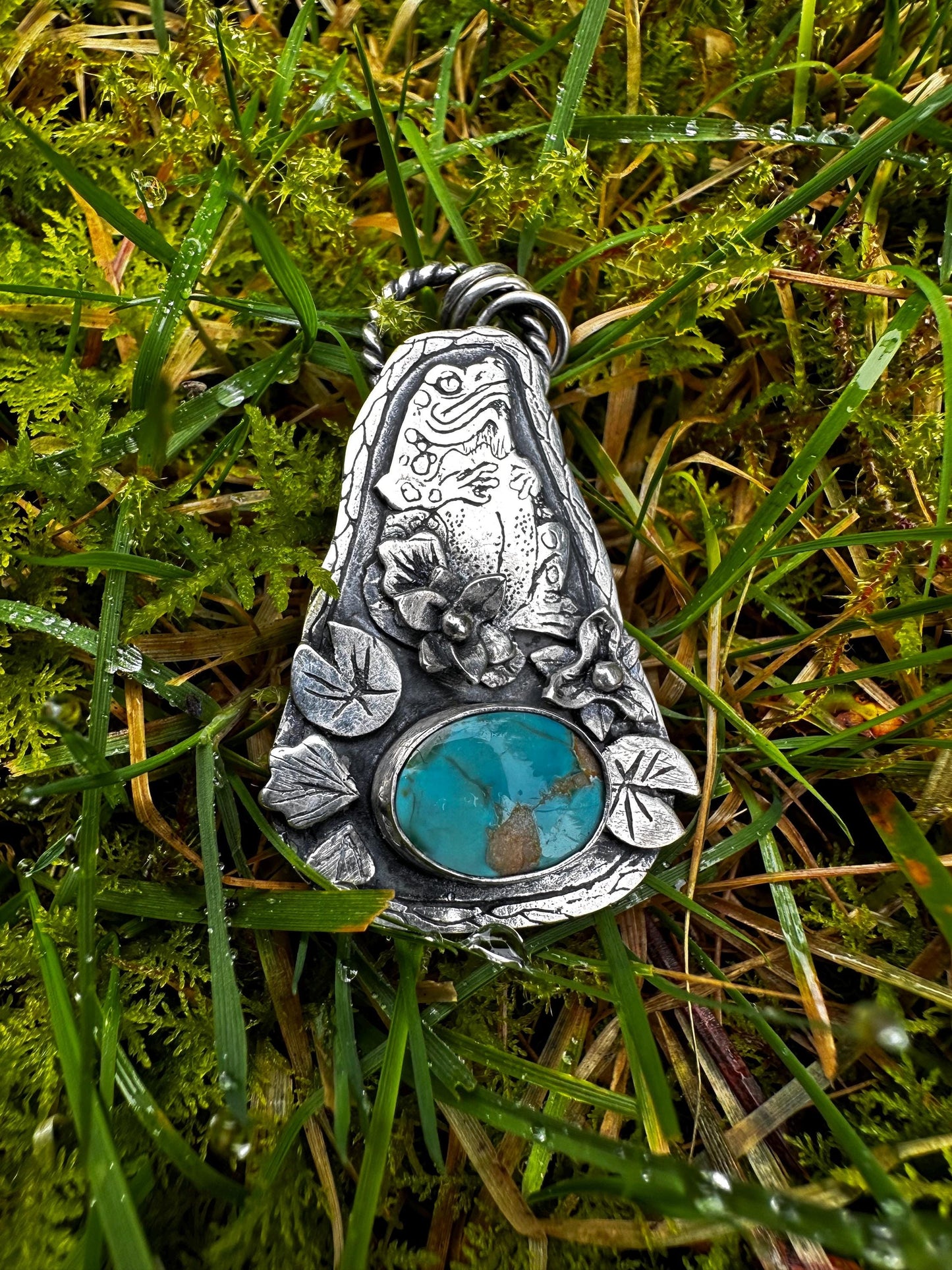 A witchy toad familiar pendant, sterling silver and finely detailed. Embellished with a botanical theme of Lilly pads, flowers and a brightly coloured and rare natura Carco Lake turquoise.