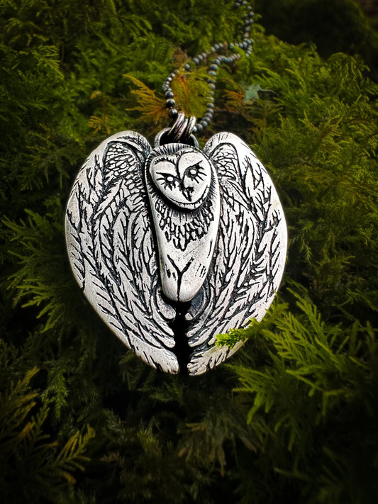 A stylied barn owl with outspread wings. Adorned with intricate detail, the barn owl is handmade in sterling silver. With an antique effect patina and polished.