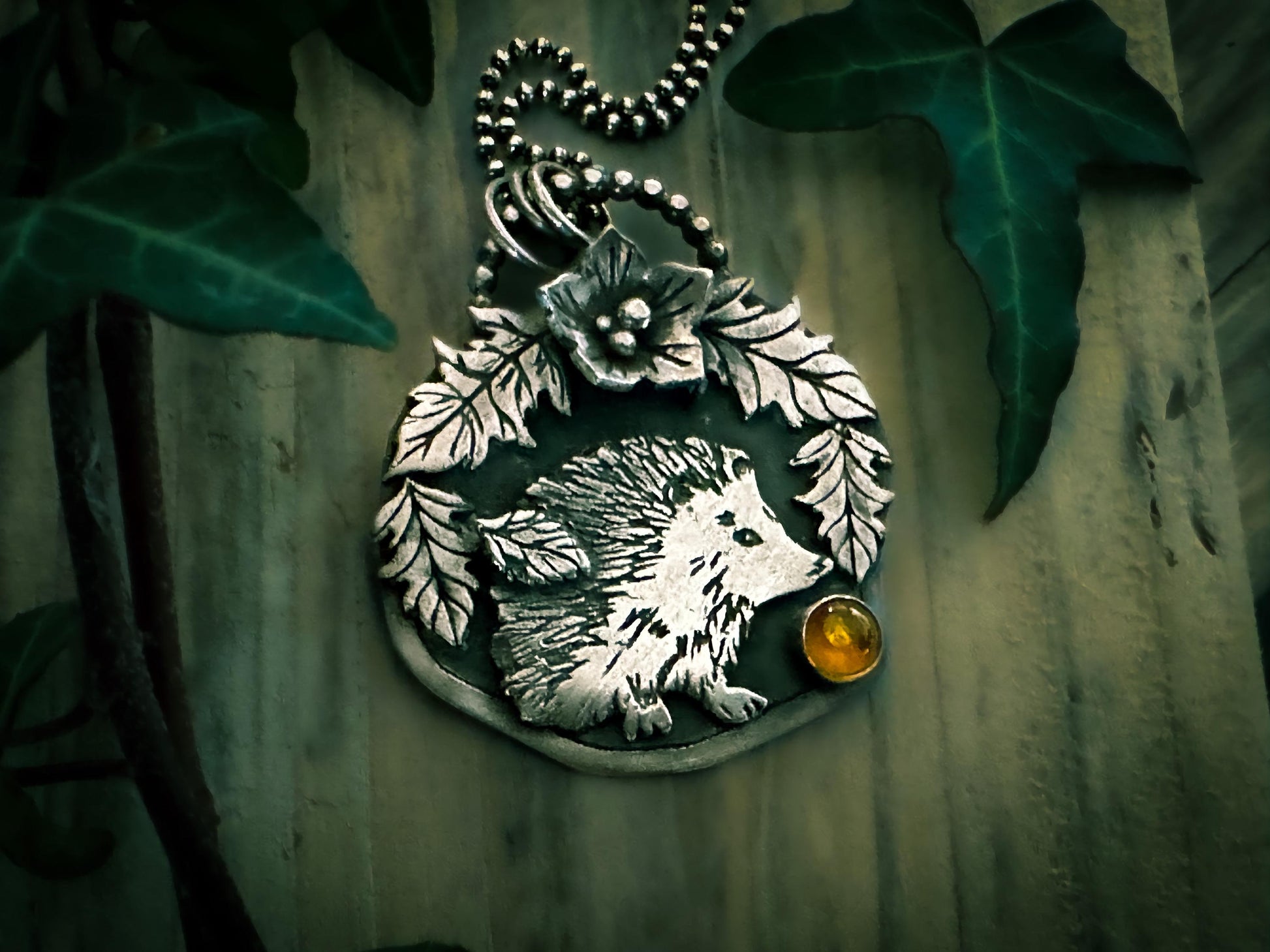 Woodland hedgehog with leaves, flowers and amber handmade in sterling silver on an oxidised back plate