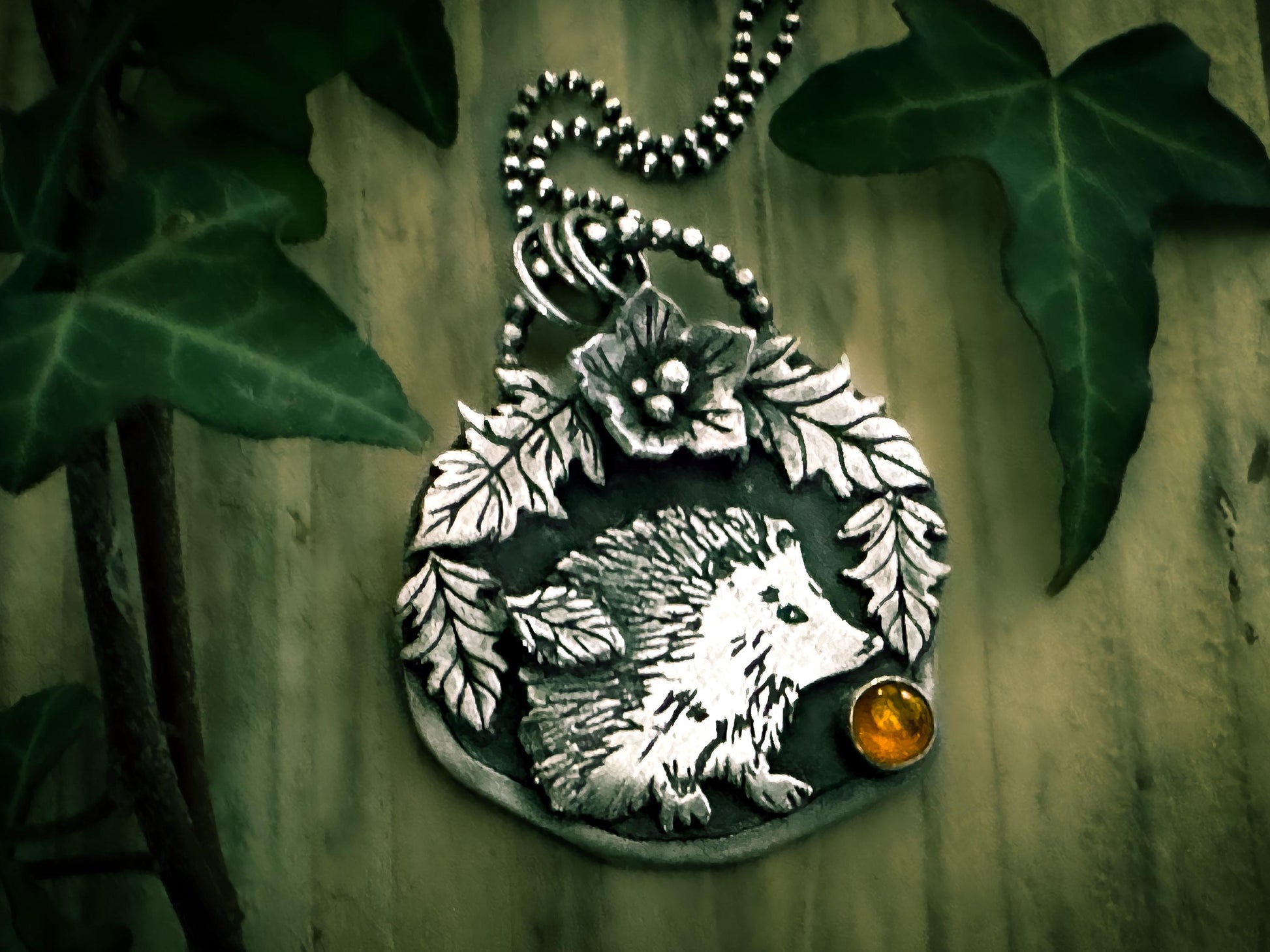 Sweet hedgehog pendant from the Little Familiars Collection, with fine details. Botanical details, and an amber cabochon. By Silver Labyrinth Jewelry