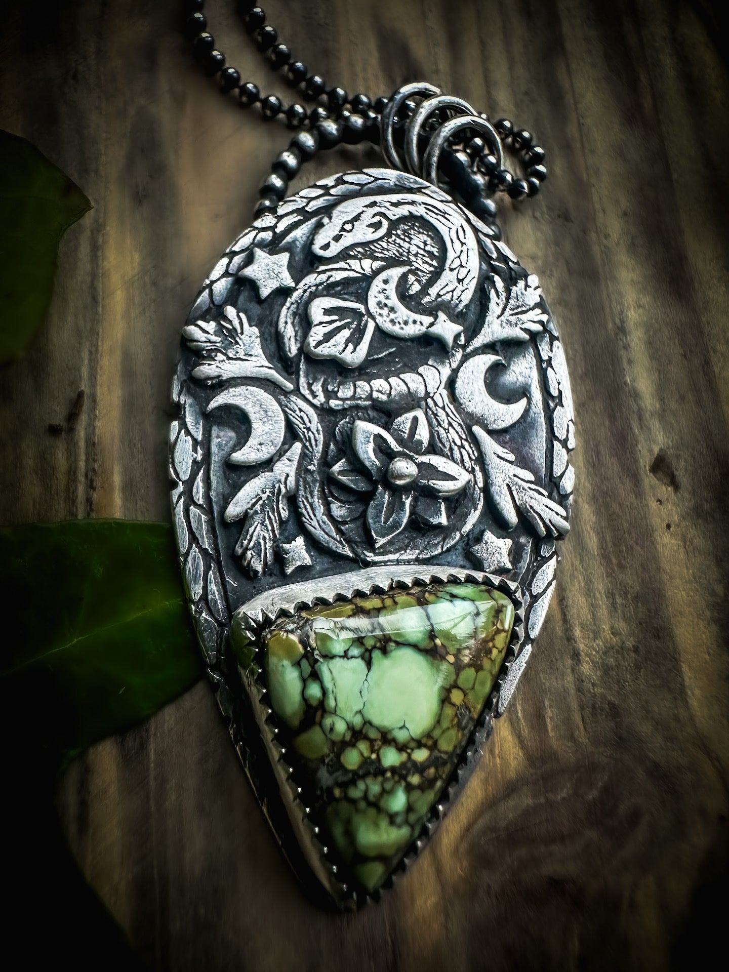 Handmade sterling silver snake pendant with high detail featuring a rare Damele variscite cabochon, nestled among leaves and flowers